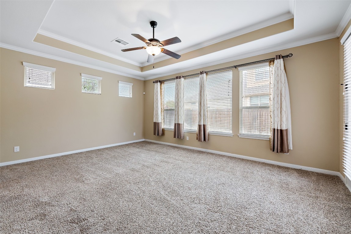 2000 Manada Trail Leander, TX 78641 - Photo 18 of 36 A spacious bedroom features a tray ceiling, ceiling fan, and carpeted flooring for comfort.