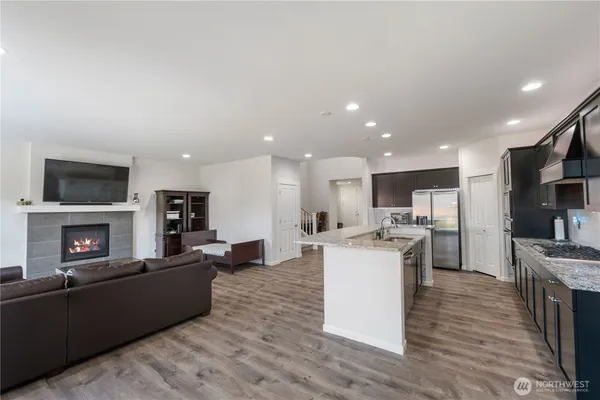 a living room with stainless steel appliances furniture a fireplace a flat screen tv and a kitchen view
