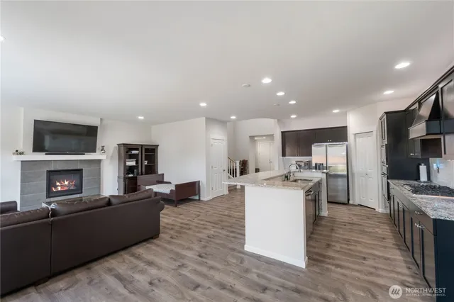 a living room with stainless steel appliances furniture a fireplace a flat screen tv and a kitchen view