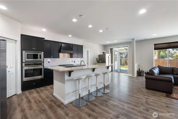 a kitchen with stainless steel appliances kitchen island granite countertop a refrigerator a stove a microwave oven a sink with white cabinets and wooden floor