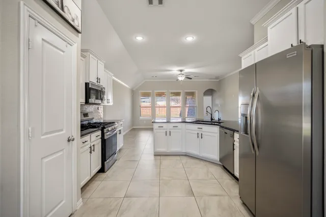 a large kitchen with a refrigerator a sink dishwasher a stove and white cabinets with wooden floor