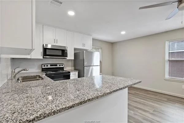 a kitchen with granite countertop a sink a counter space appliances and cabinets