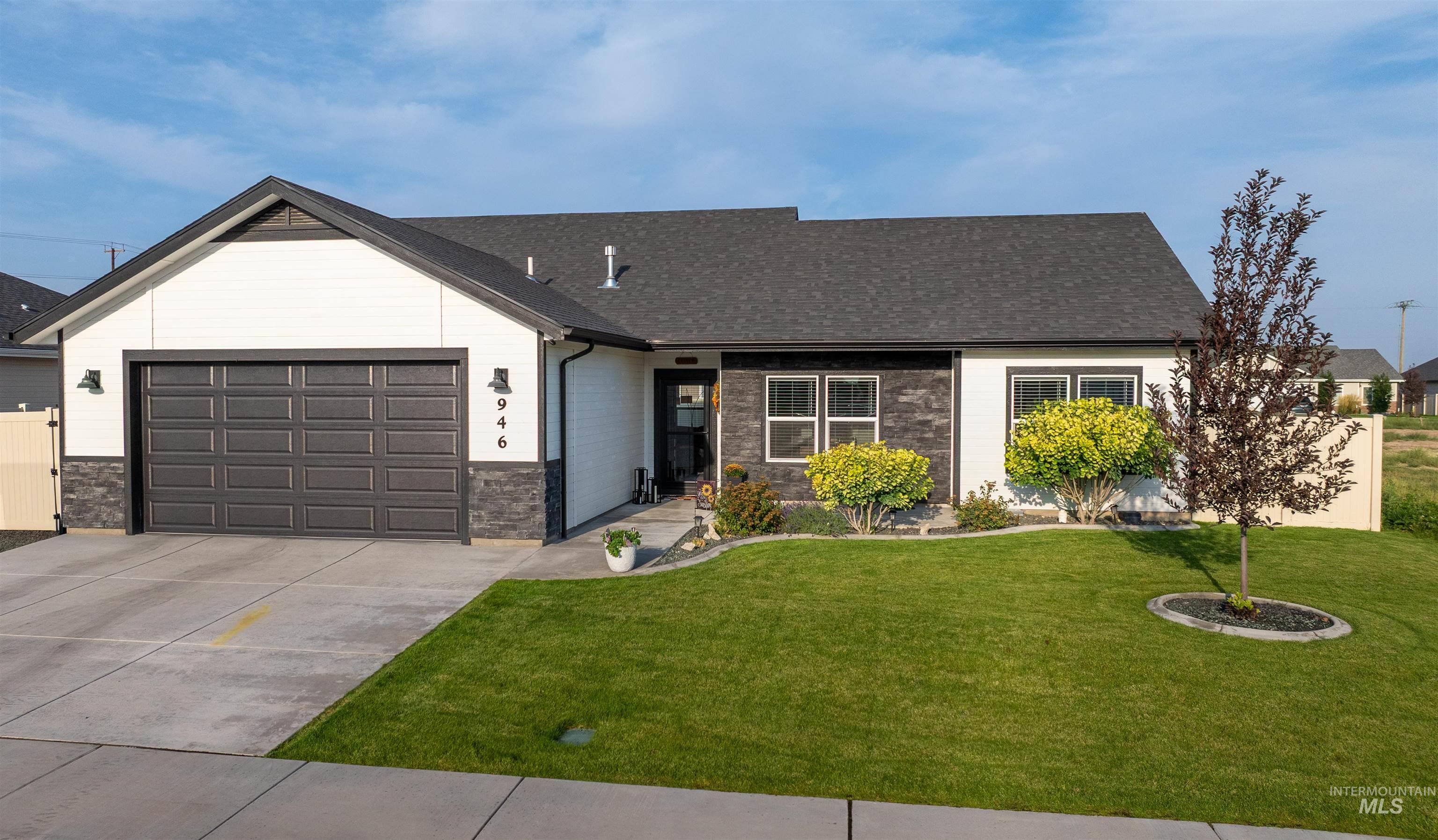 View of front of property featuring an attached garage, a front lawn, driveway, stone siding, and roof with shingles