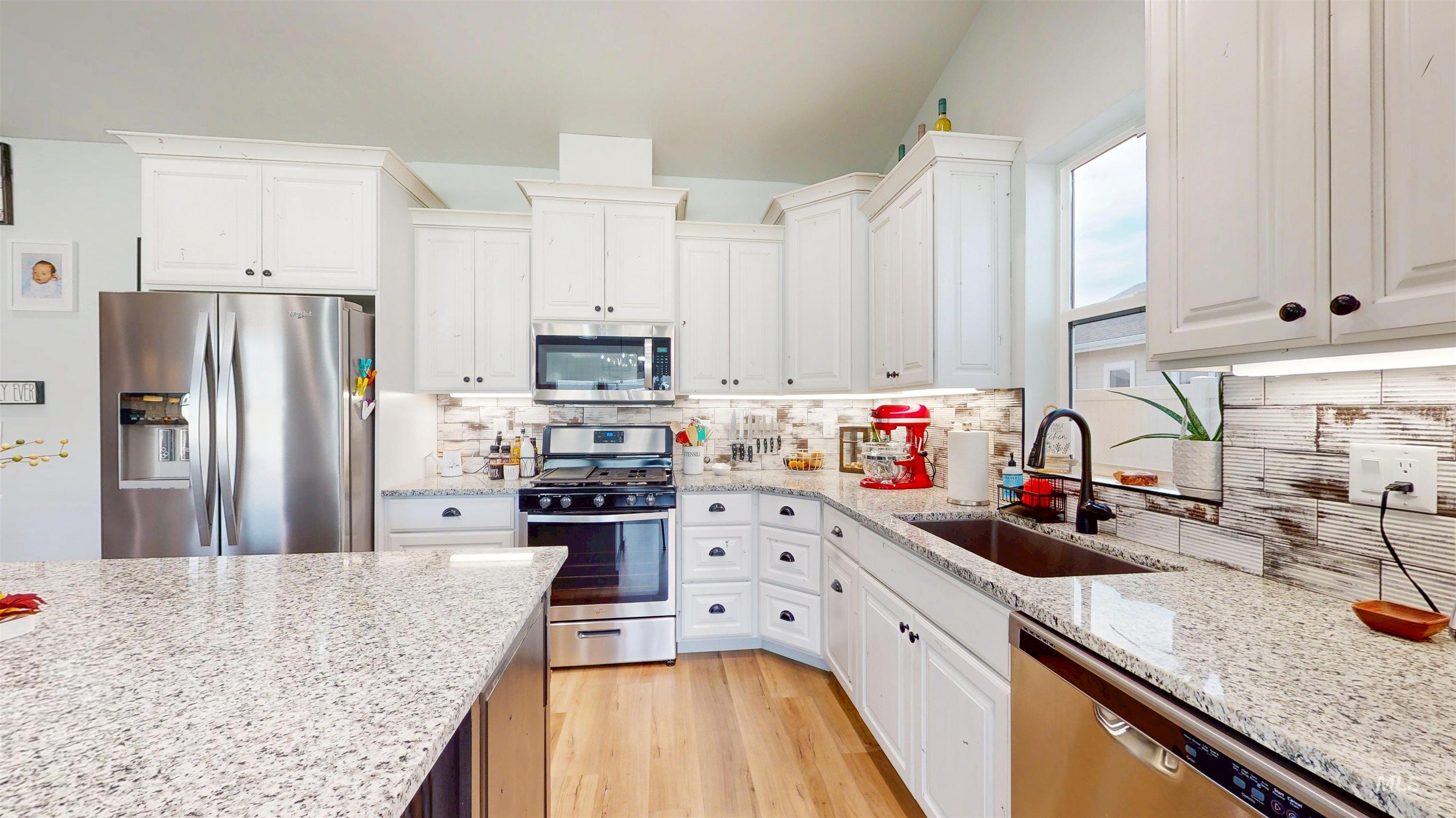946 Kenbrook Loop Twin Falls, ID 83301 - Photo 18 of 35 Kitchen featuring appliances with stainless steel finishes, tasteful backsplash, white cabinets, and light stone countertops