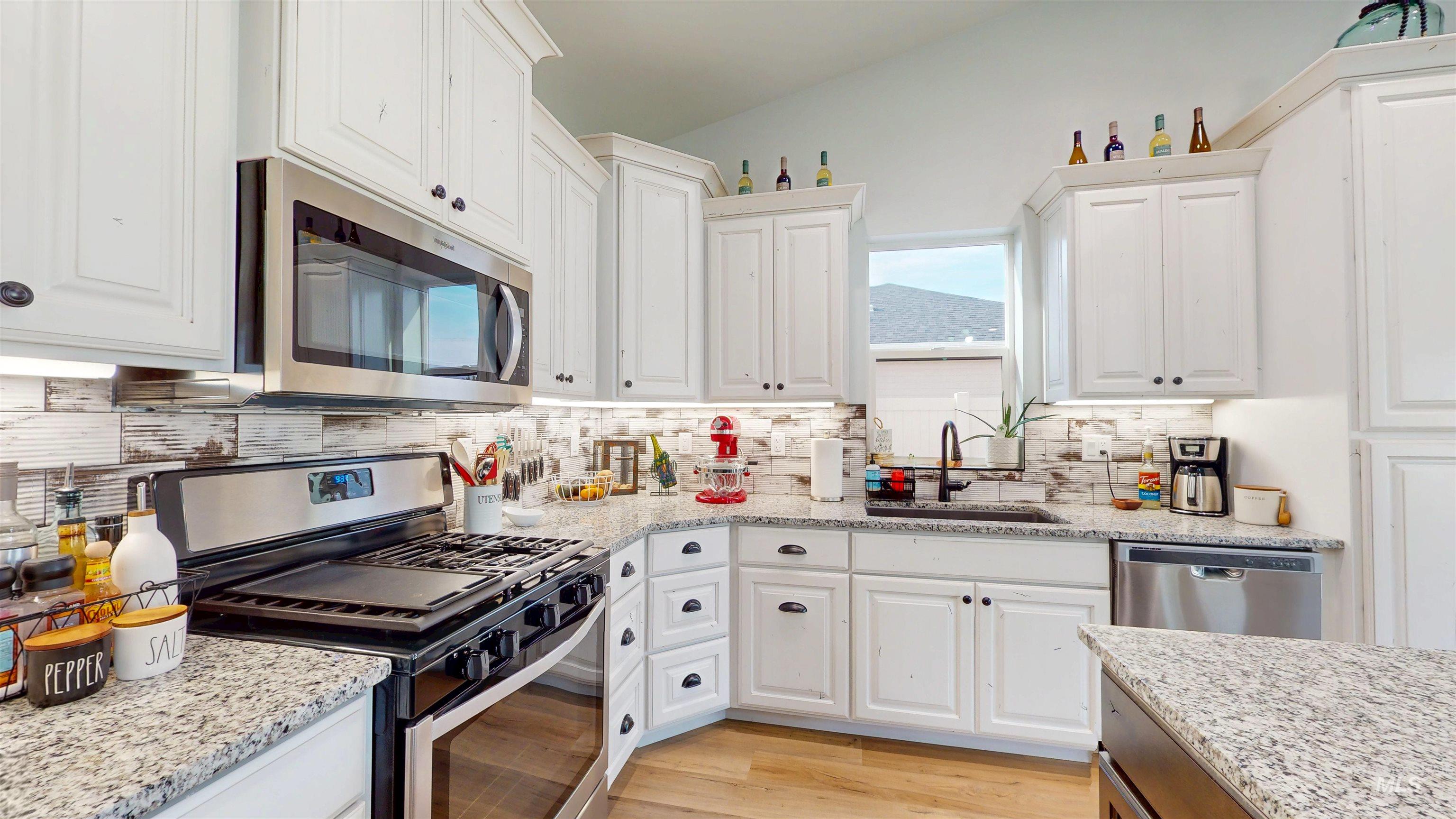 946 Kenbrook Loop Twin Falls, ID 83301 - Photo 3 of 35 Kitchen with stainless steel appliances, white cabinets, backsplash, light wood-style floors, and light stone counters