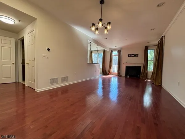 a view of an empty room with wooden floor and a kitchen