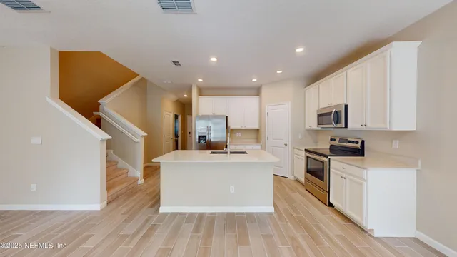 a large kitchen with stainless steel appliances granite countertop a stove top oven a sink dishwasher and a refrigerator with wooden floor