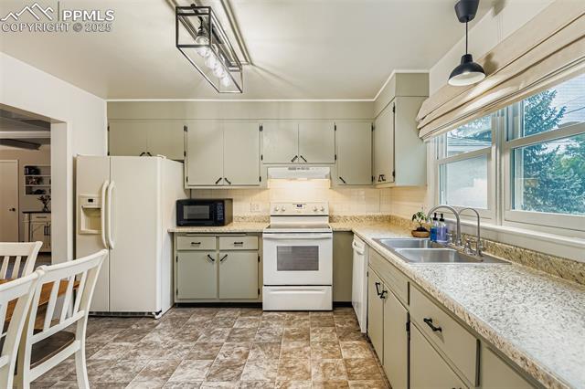 2462 Lafayette Road Colorado Springs, CO 80907 - Photo 8 of 22 Kitchen featuring white appliances, tasteful backsplash, under cabinet range hood, stone finish flooring, and decorative light fixtures