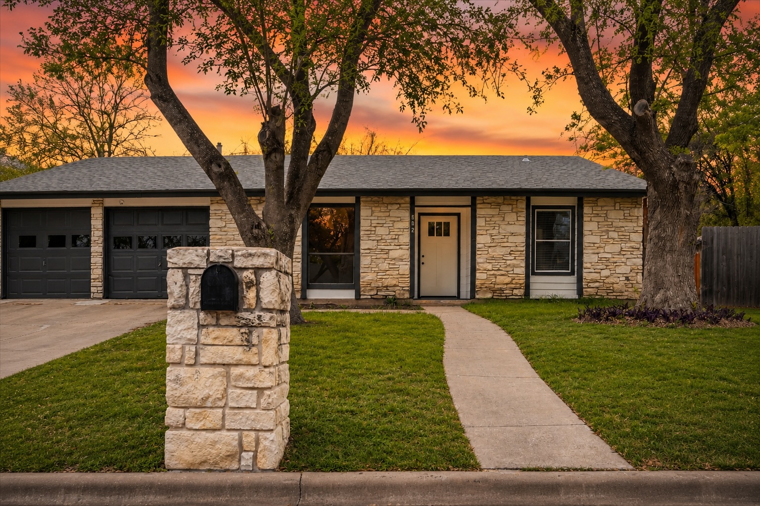 502 Pin Tail Lane Taylor, TX 76574 - Photo 1 of 26 Stone facade home featuring a two-car garage, a concrete walkway, a stone mailbox pillar, and mature trees