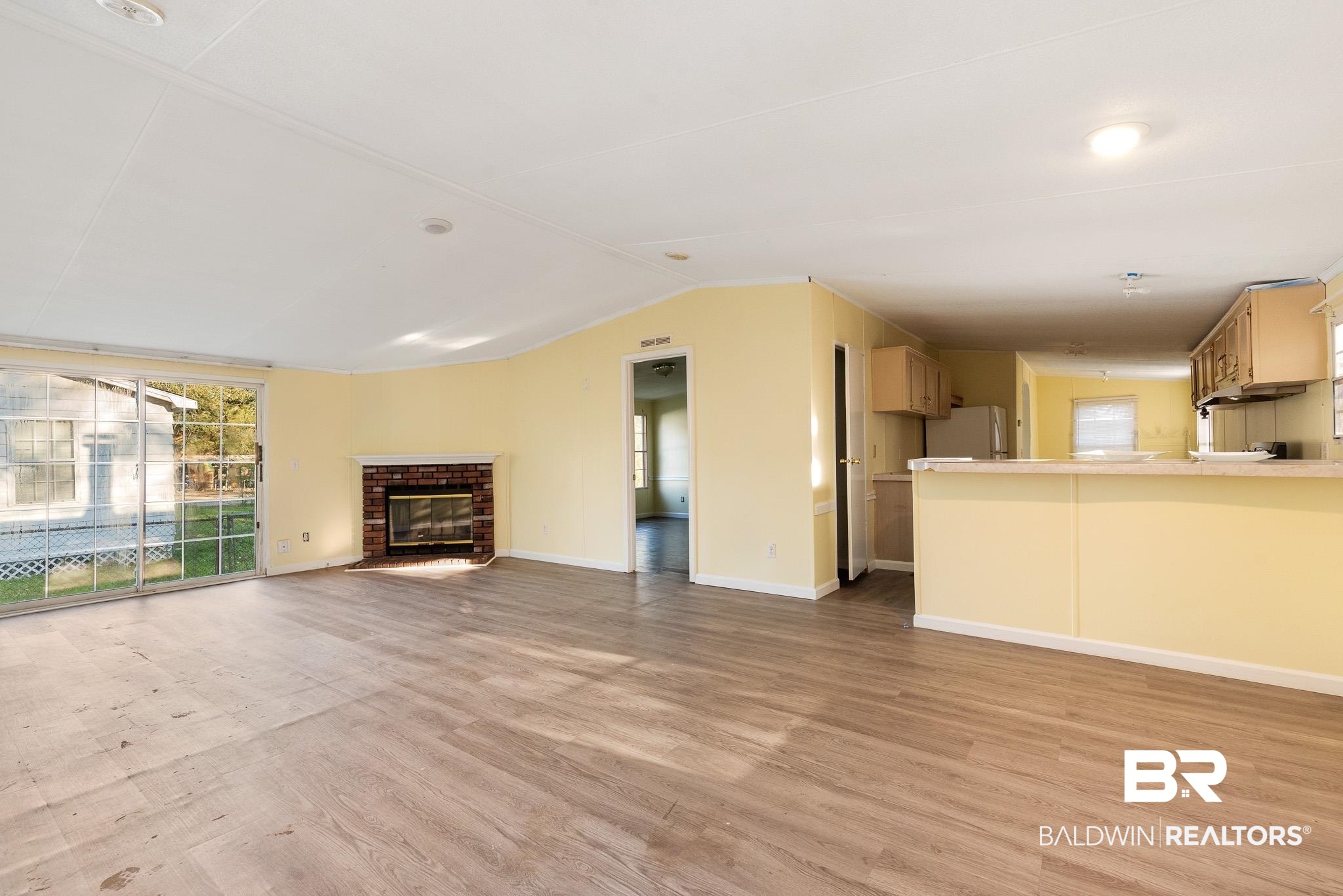 7695 Bermuda Drive Semmes, AL 36575 - Photo 7 of 27 Unfurnished living room featuring light wood-style flooring, a fireplace, baseboards, and vaulted ceiling