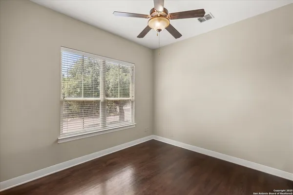 an empty room with wooden floor fan and windows