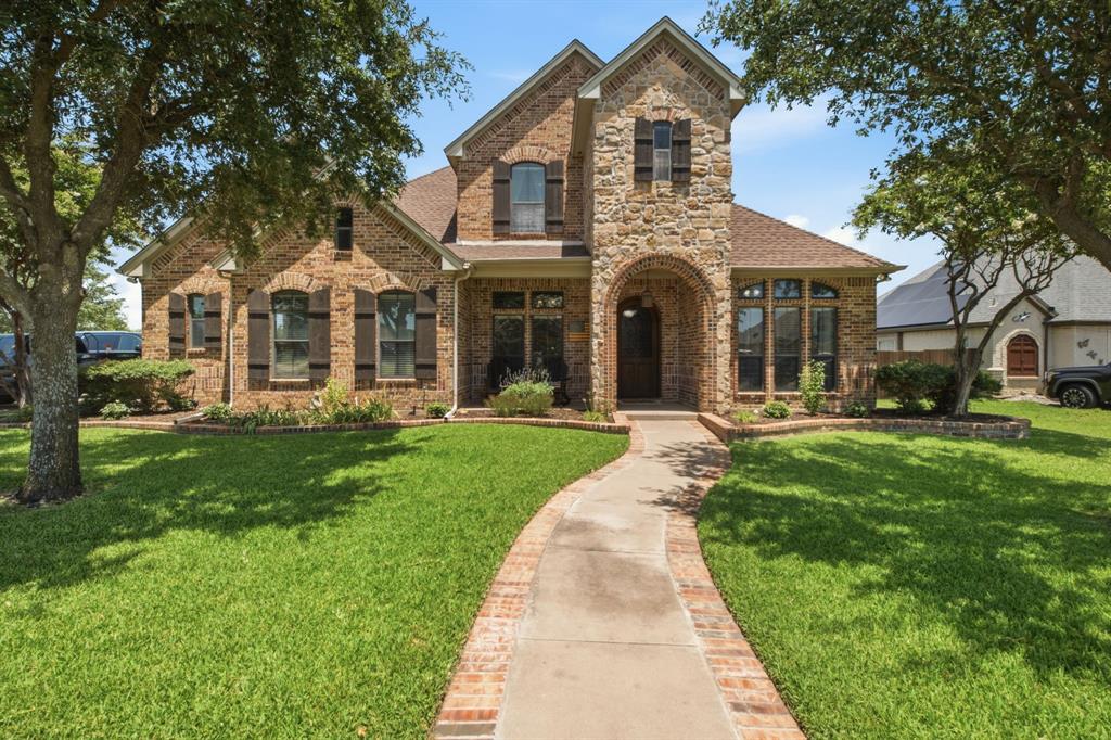600 Aspen Street Pilot Point, TX 76258 - Photo 39 of 39 Two-story brick and stone exterior featuring an arched entry, dark wood shutters, and a front pathway bordered by brick
