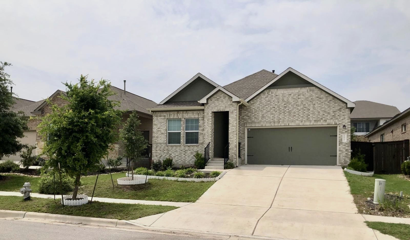 Single-story residence featuring a brick exterior with a pitched roof, an attached two-car garage, a concrete driveway, and a landscaped front yard with young trees