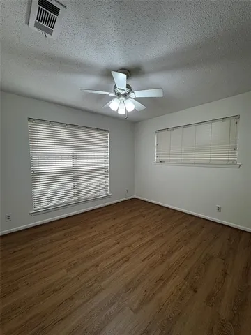 an empty room with wooden floor chandelier fan and windows