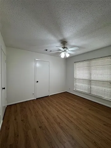 an empty room with wooden floor fan and windows