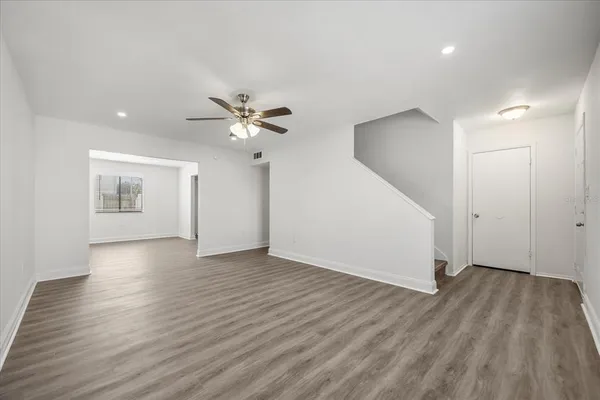a view of an empty room with wooden floor and a ceiling fan
