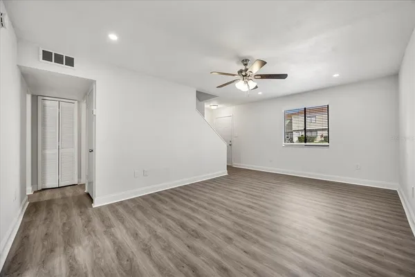 an empty room with wooden floor ceiling fan and windows