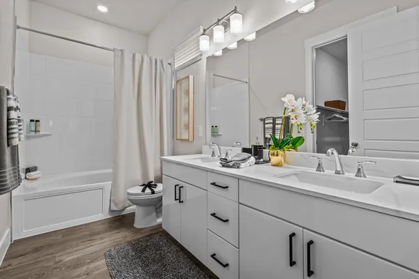 a bathroom with a double vanity sink a toilet a mirror and shower