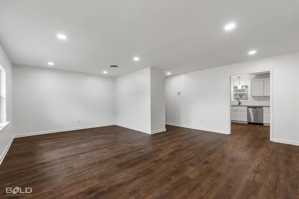 a view of an empty room with wooden floor and a kitchen