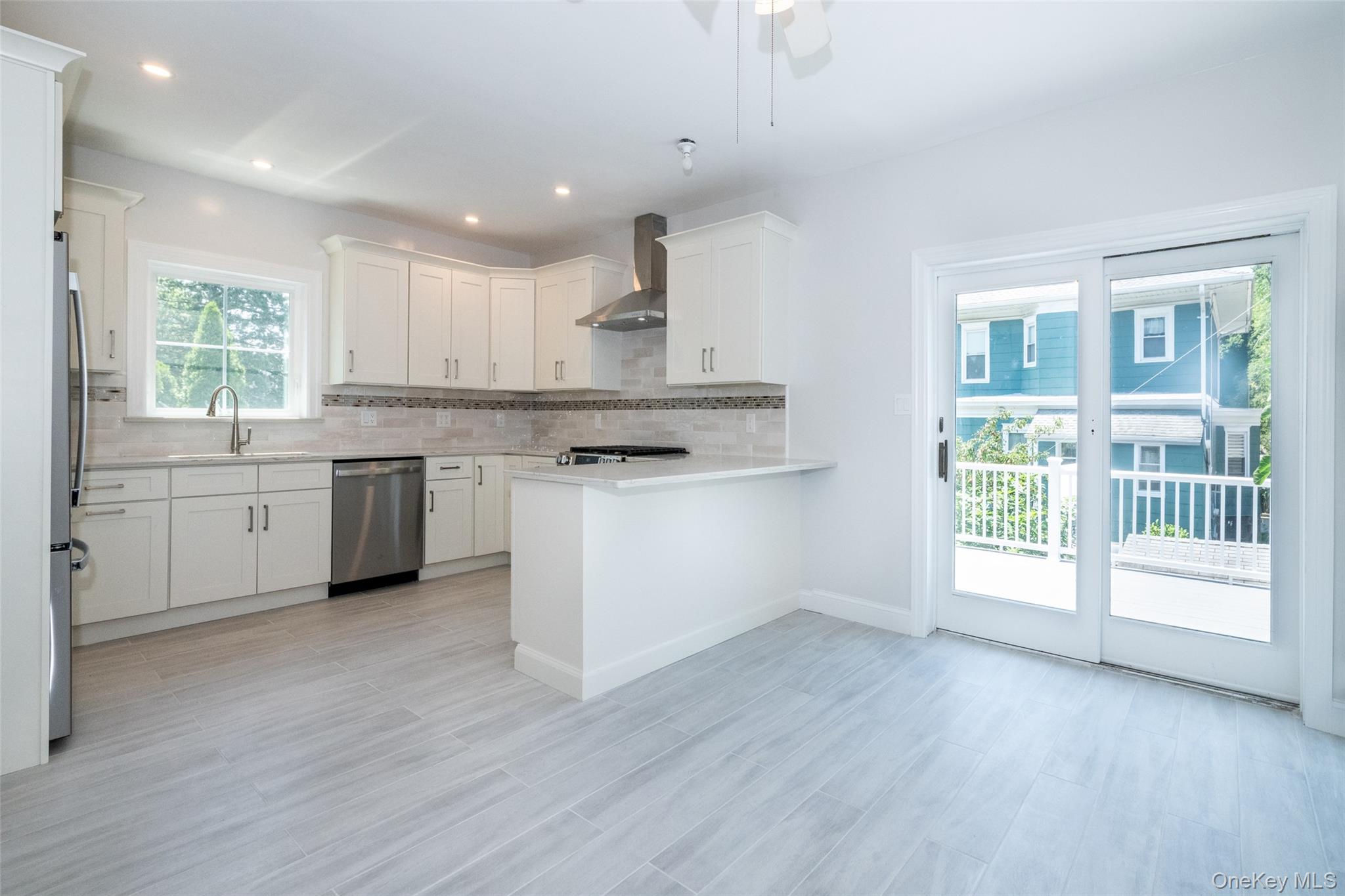 7 Alpha Place, Unit FIRST New Rochelle, NY 10805 - Photo 8 of 25 Kitchen with stainless steel appliances, wall chimney exhaust hood, light countertops, backsplash, and white cabinetry