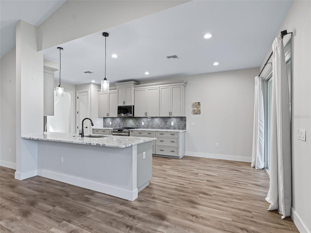 562 Dowling Circle Lady Lake, FL 32159 - Photo 12 of 62 a kitchen with stainless steel appliances granite countertop a sink a stove a refrigerator and island with wooden floor