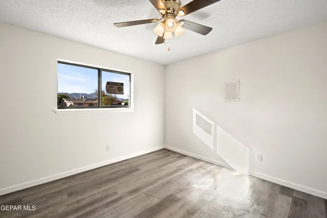 an empty room with wooden floor chandelier fan and windows
