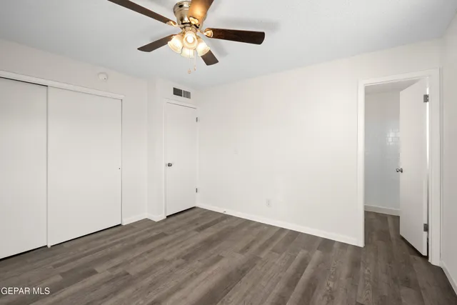 an empty room with wooden floor a ceiling fan & windows