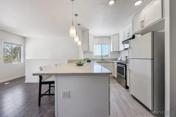 a kitchen with kitchen island a refrigerator a stove a sink dishwasher and white cabinets with wooden floor