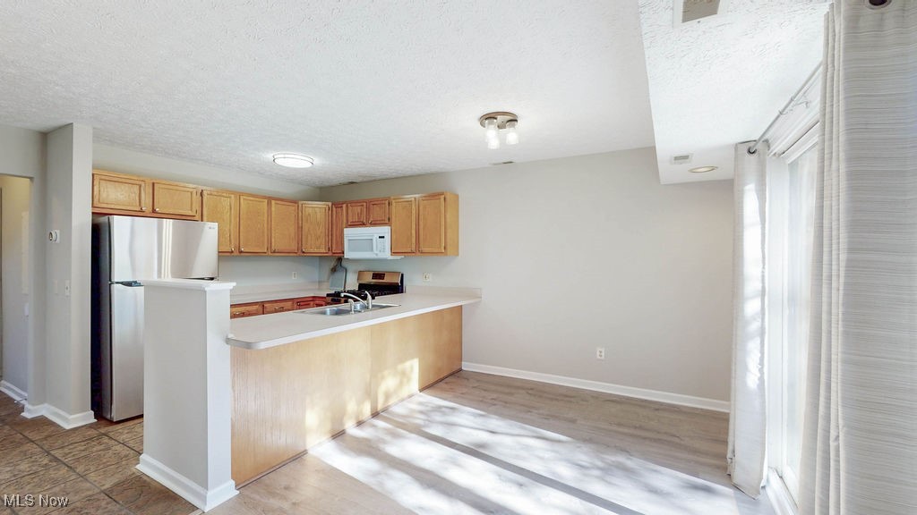 1426 Loop Road, Unit 1426 Kent, OH 44240 - Photo 10 of 40 Kitchen with appliances with newer appliances, light countertops, a textured ceiling, a peninsula, and light wood-style floors. Open to the dining room.