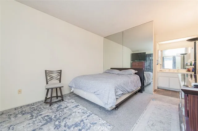 a bedroom with a bed a chair and potted plant on the dresser