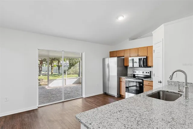 a kitchen with stainless steel appliances granite countertop a refrigerator a stove a sink a dining table and chairs with wooden floor