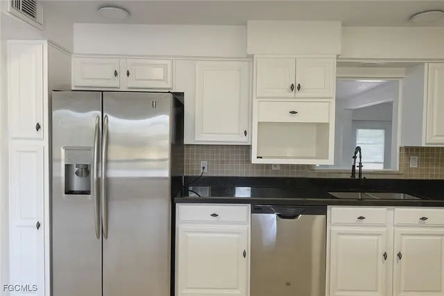 a kitchen with stainless steel appliances granite countertop a refrigerator a sink a stove and white cabinets