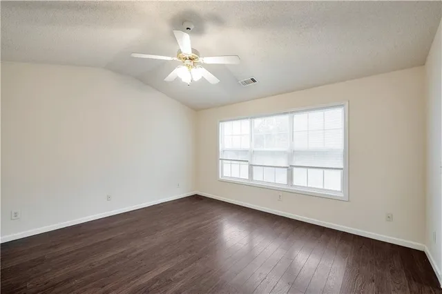 an empty room with wooden floor fan and windows