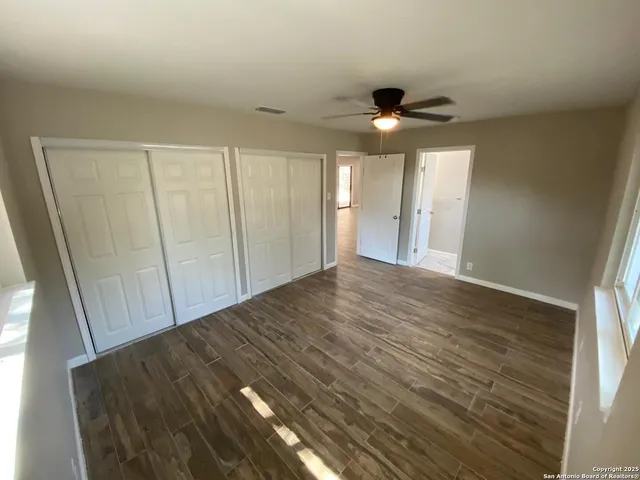 an empty room with wooden floor fan and windows