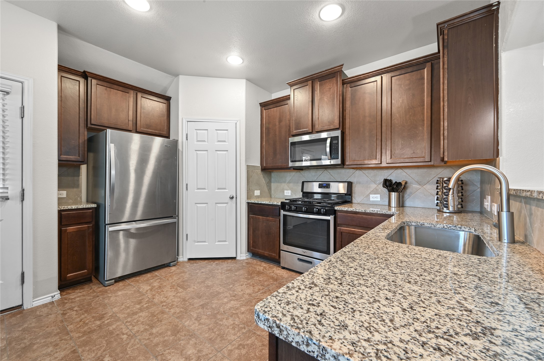 303 Limerick Road Buda, TX 78610 - Photo 7 of 23 Kitchen featuring granite countertops, stainless steel appliances, dark wood cabinetry, a tile backsplash, and recessed lighting