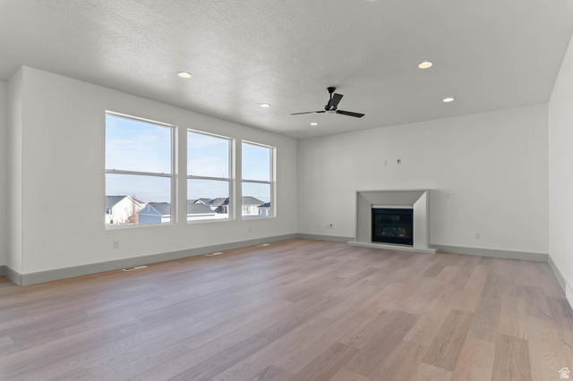 562 West Coyote Rdg Road Grantsville, UT 84029 - Photo 10 of 27 Spacious room featuring multiple large windows, wood-finish flooring, a contemporary fireplace with a stone surround, and recessed lighting