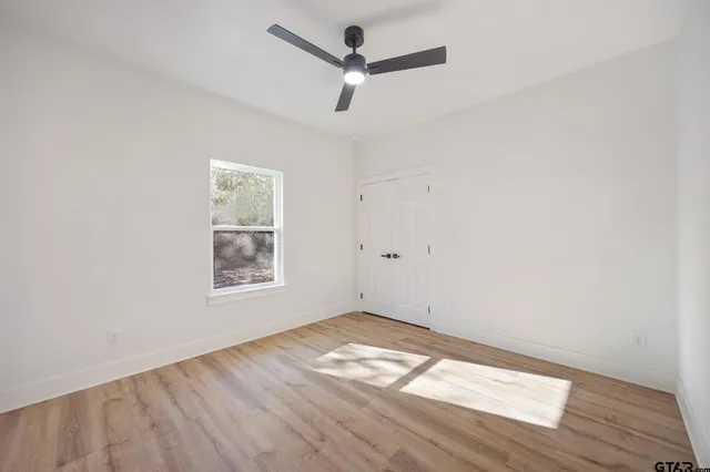 an empty room with wooden floor ceiling fan and window