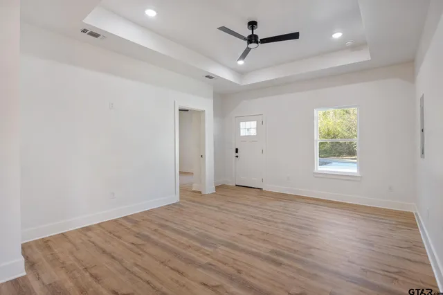 an empty room with wooden floor ceiling fan and windows
