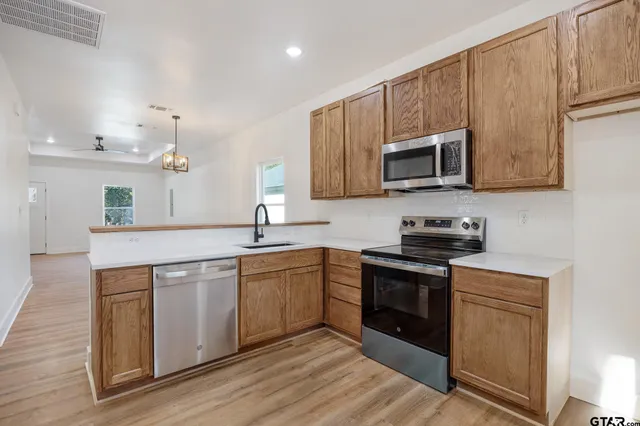 a kitchen with stainless steel appliances granite countertop a stove top oven a sink dishwasher and a microwave oven on the wooden floor