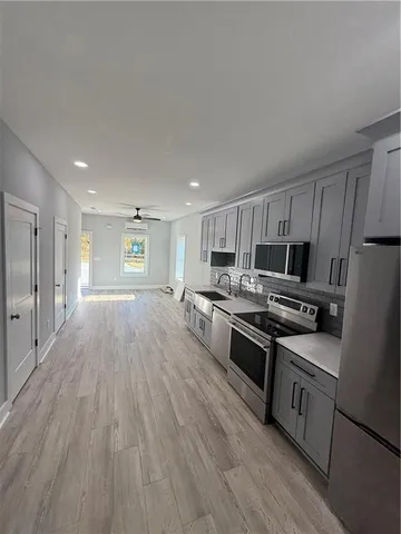 a kitchen with stainless steel appliances a stove top oven a sink dishwasher and a refrigerator with wooden floor