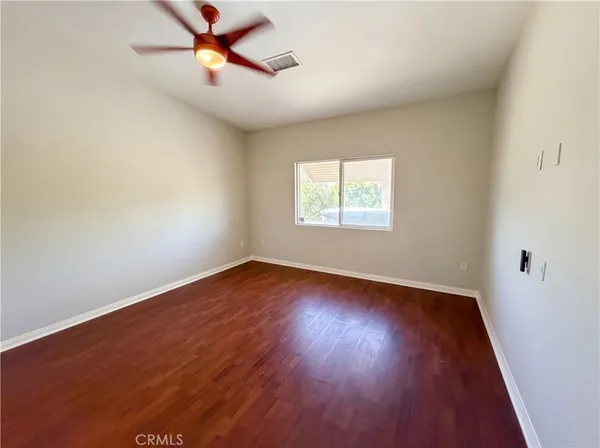 an empty room with wooden floor ceiling fan and windows