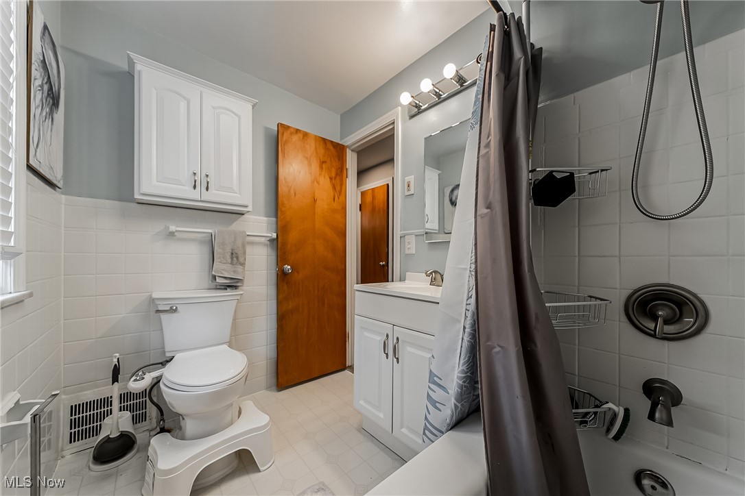 1235 Dorsh Road Cleveland, OH 44121 - Photo 21 of 39 Full bath with tile walls, vanity, shower / bathtub combination with curtain, and wainscoting