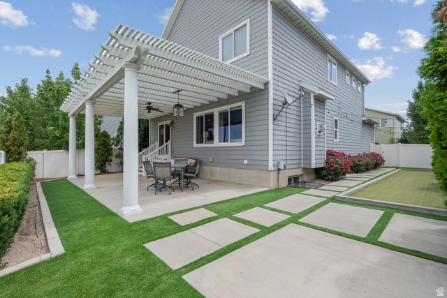955 Delorean Lane Midvale, UT 84047 - Photo 40 of 47 Rear exterior featuring a white pergola over a paved patio, a gray siding facade, and a synthetic turf lawn with paver stepping stones
