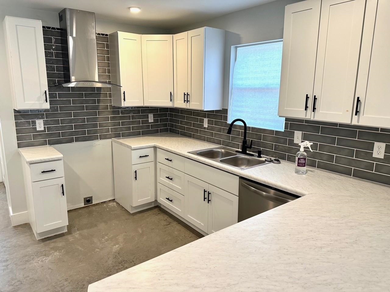 853 Hanley Street Memphis, TN 38114 - Photo 5 of 12 Kitchen featuring wall chimney range hood, backsplash, white cabinets, stainless steel dishwasher, and concrete floors