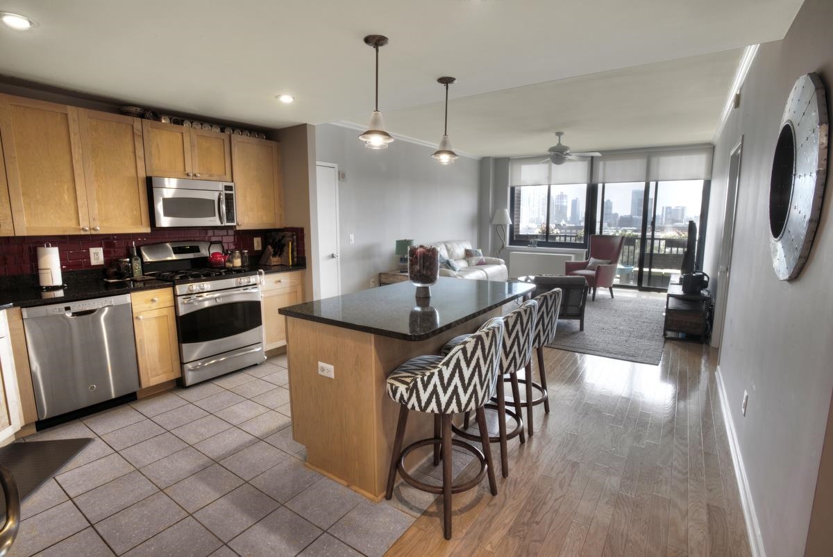 700 Grove Street, Unit 12J Jersey City, NJ 07310 - Photo 4 of 16 a kitchen with stainless steel appliances granite countertop a stove a sink a microwave a center island and furniture