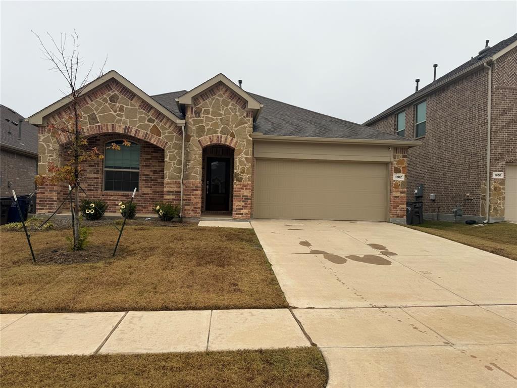 View of front of house featuring stone siding, concrete driveway, an attached garage, brick siding, and roof with shingles