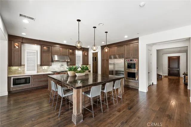 a kitchen with stainless steel appliances granite countertop a stove top oven a sink a dining table and chairs with wooden floor