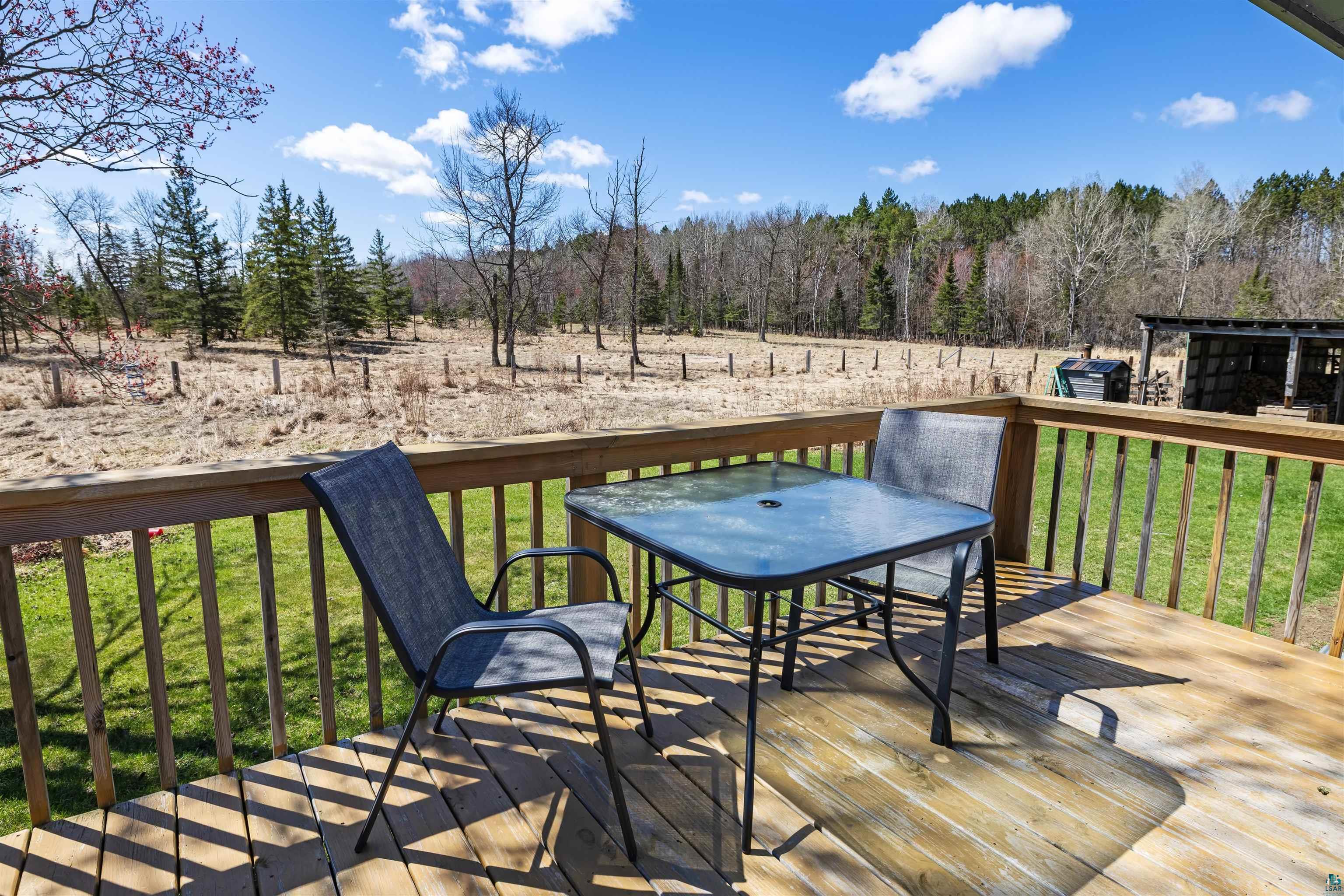 40139 County Road 251 Cohasset, MN 55721 - Photo 29 of 50 Expansive exterior deck featuring natural wood decking and railing, overlooking a fenced, undeveloped property with mature trees bordering the perimeter