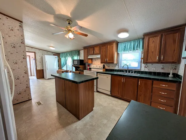 a kitchen with stainless steel appliances granite countertop a refrigerator a sink dishwasher a stove and white countertops with wooden floor