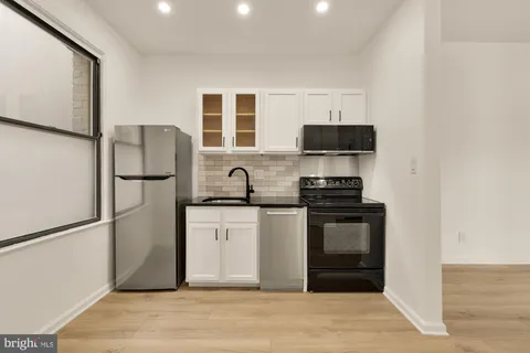 a kitchen with stainless steel appliances granite countertop a stove a refrigerator a sink a dining table and chairs with wooden floor